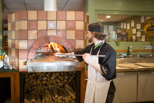 Chef placing a pizza in the wood-fired oven at the Hearth & Vine Cafe.