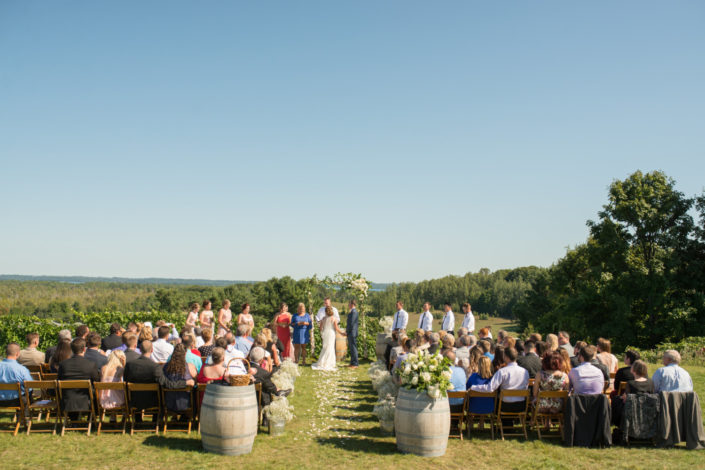 Wedding ceremony with bride and groom and guests at the scenic hilltop vineyard.