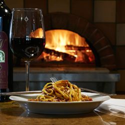 Image of pasta and a glass of red wine in front of the wood-fired oven at the Hearth & Vine Cafe