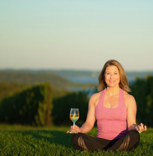 Yoga instructor with a glass of wine in a vineyard.