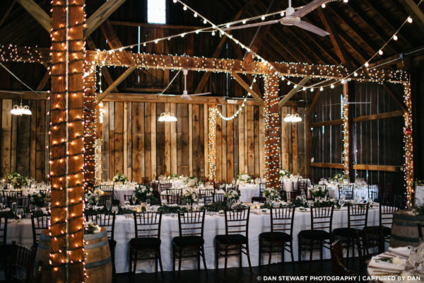 Beautiful wedding reception tables in the Pegasus Barn with lights wrapped around the beams.
