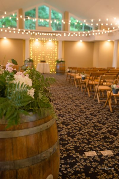 Wedding ceremony set up with chairs, alter, wine barrels, flowers, and lights.