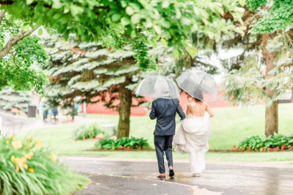 Bride and groom walking in the rain with umbrellas.
