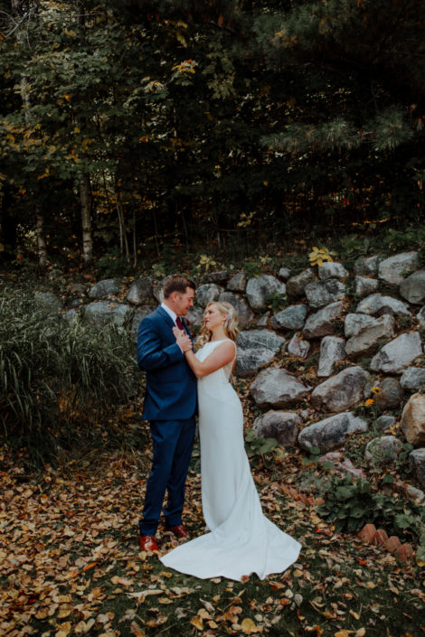 Bride and groom standing among fall leaves in front of the rock wall.