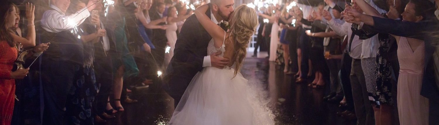 Bride and groom kissing in front of the Pegasus Barn with guests holding lit sparklers.