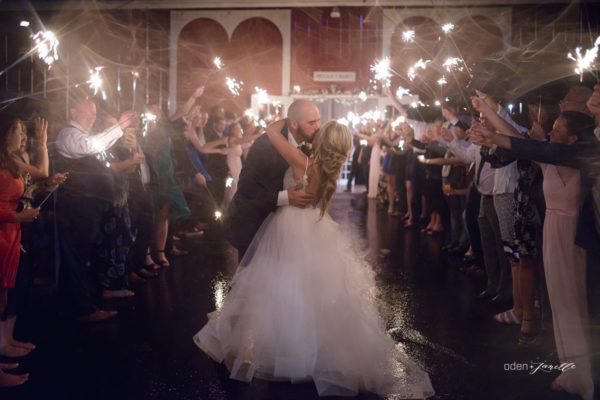 Bride and groom kissing in front of the Pegasus Barn with guests holding lit sparklers.