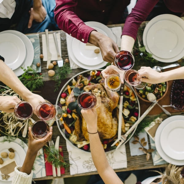 People clinking glasses of wine over a Thanksgiving dinner table.