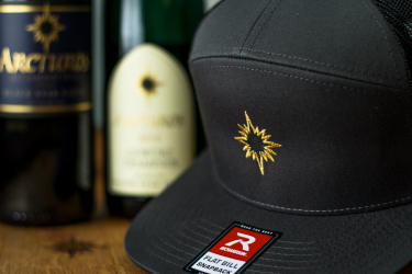 Photo of a Black Star Farms Flat-Bill Hat and a bottle of Cabernet Franc and Gewurztraminer