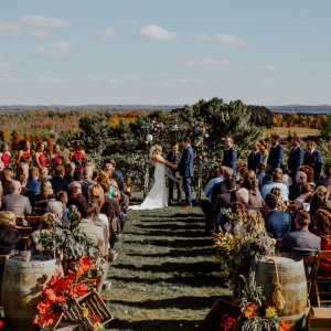 Fall wedding ceremony with bride, groom, officiant, and attendees atop our vineyard.