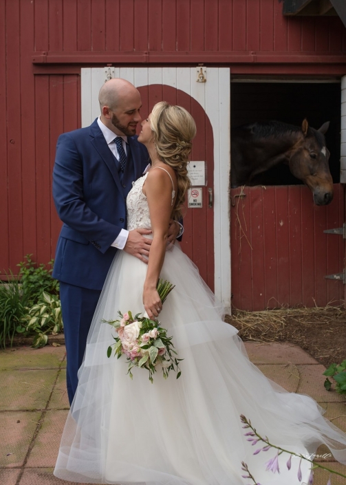Bride and groom with a horse in a barn at the stables at Black Star Farms.