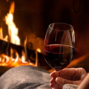 Women lounging by the fireplace with red wine.
