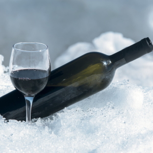 Glass and bottle of red wine in the snow.