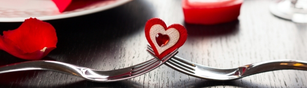 Two forks holding a heart on a Valentine's decorated table.