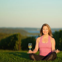 Yoga instructor by a vineyard with a glass of wine.