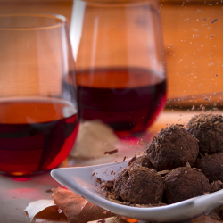 Two red wine glasses with a plate of chocolate truffles.