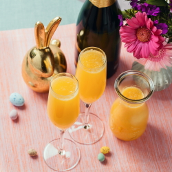 Two mimosas with a bottle of sparkling wine, OJ, and Easter decorations.