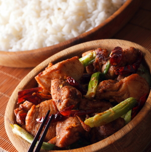 A bowl of Kung Pao Chicken with white rice in the background.
