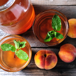 Two glasses of brandy peach tea with fresh peaches on the side.