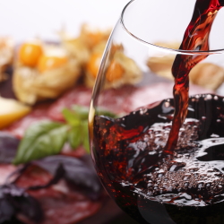 Pouring a glass of red wine with food in the background.