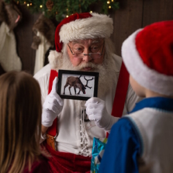 Santa showing a photo of a reindeer to a young girl and boy.