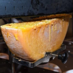 A half wheel of raclette melting under a heater.