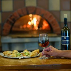 Specialty pizza in front of wood-fired oven with a glass and bottle of Cabernet Franc.