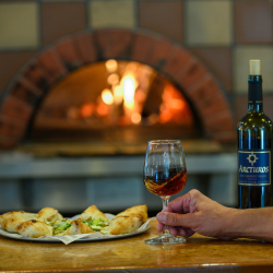 Enjoying a glass of red wine and pizza with wood-fired oven in the background.
