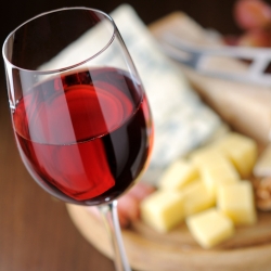 A glass of red wine with different cheeses in the background.