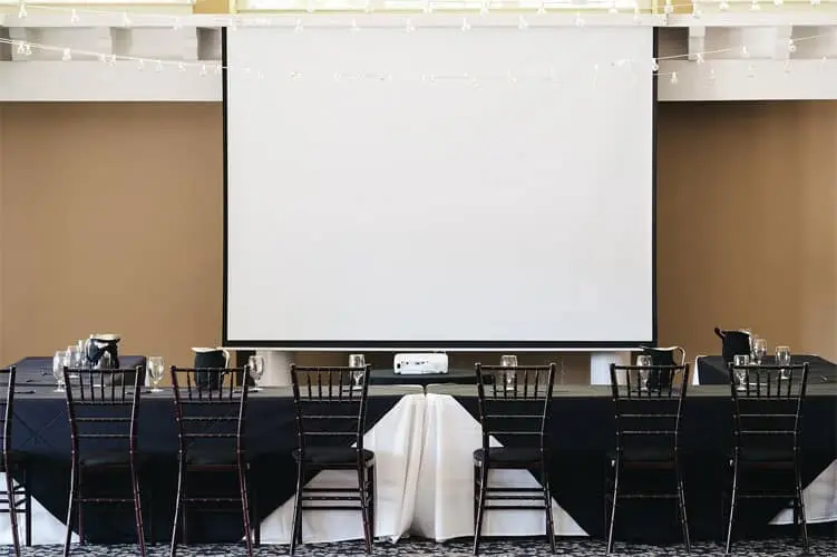 Weddings 66 Room with chairs and tables, featuring a large screen for presentations or conferences.