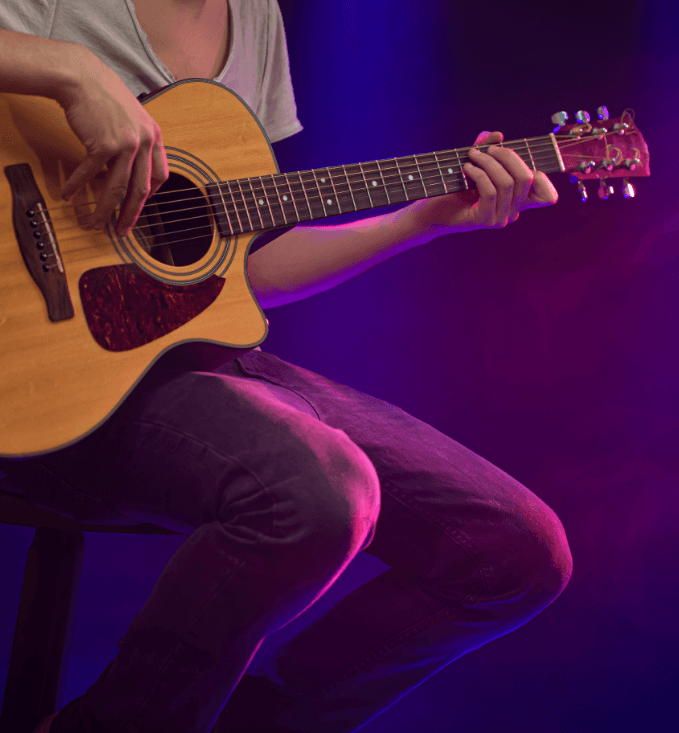 A person seated on a chair, skillfully playing an acoustic guitar, immersed in their music.