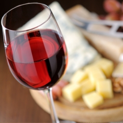 Glass of red wine with cheese in the background.