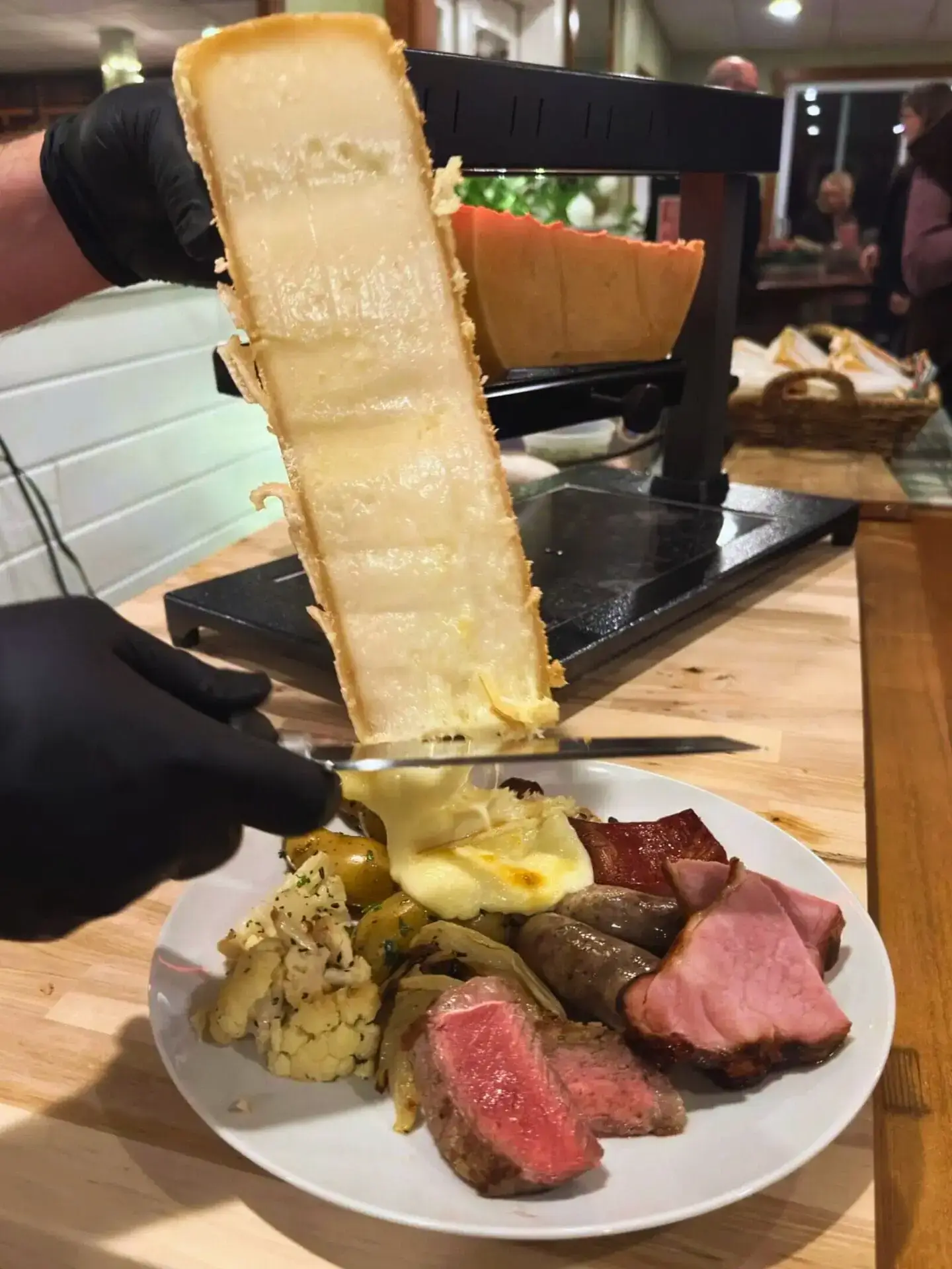 Swiss Raclette Dinner Scraping melted Raclette cheese over a dinner plate of meats and vegetables