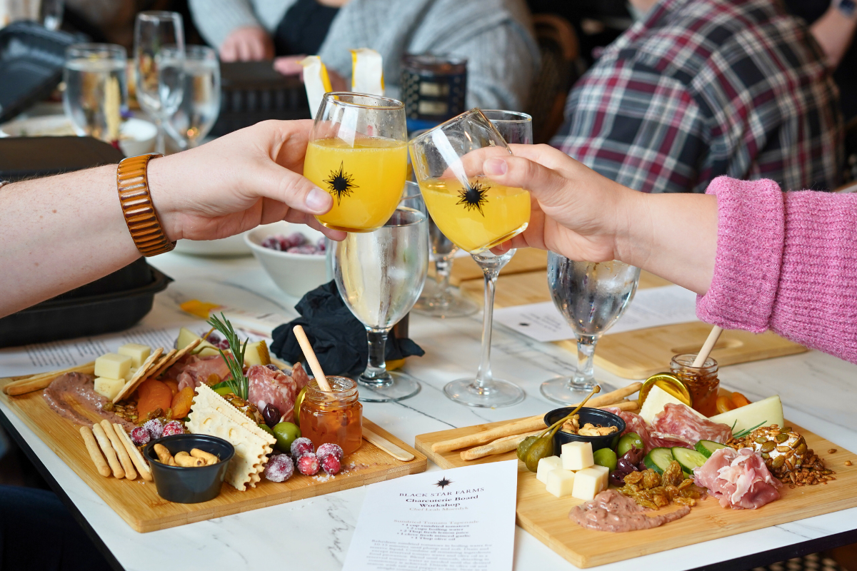 Two ladies clinking mimosas in a workshop over two charcuterie boards