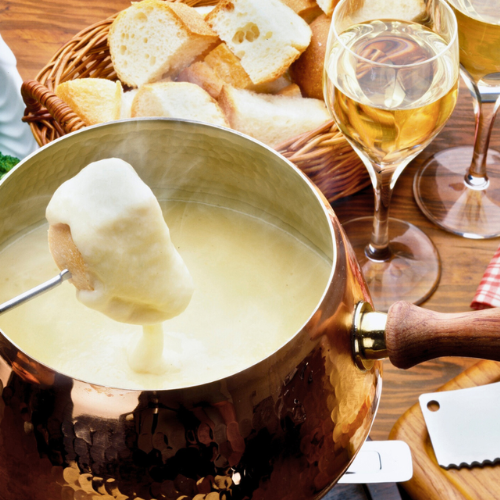 Sip & Dip Fondue Brunch Dipping fresh bread into cheese fondue with a glass of white wine.