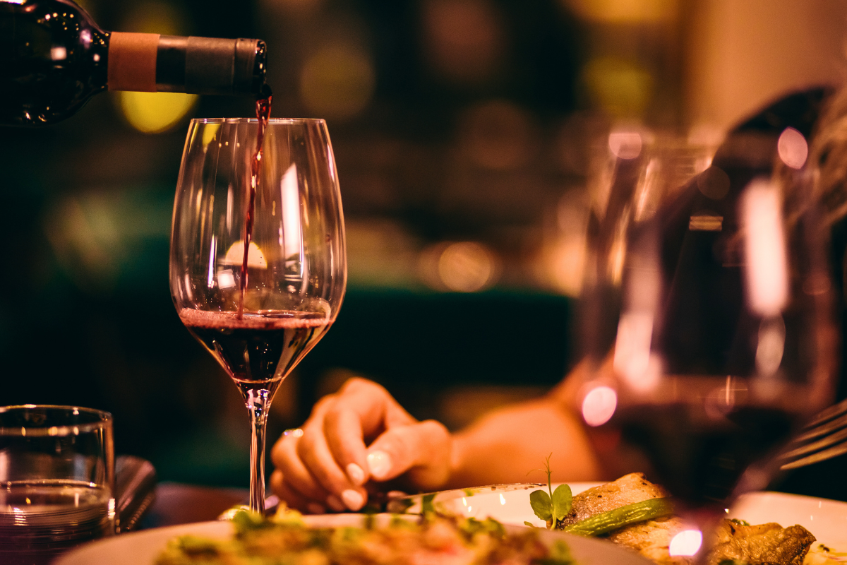 Guests dining while a glass of red wine is being poured.
