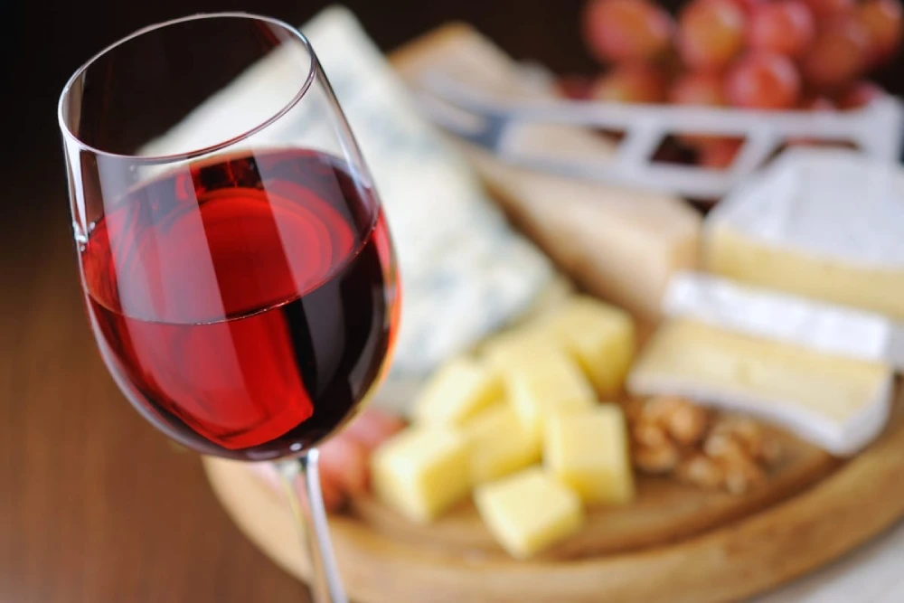 Wine & Cheese Tasting Workshop 1 Glass of red wine with different cheeses in the background.